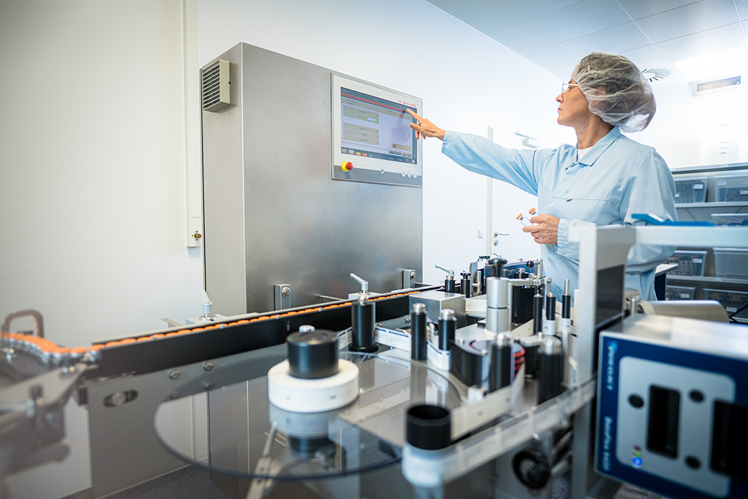 Mitarbeiter in Reinraumkleidung bedient die Etikettiermaschine bei der GMP-Herstellung von Cold Kits bei ROTOP