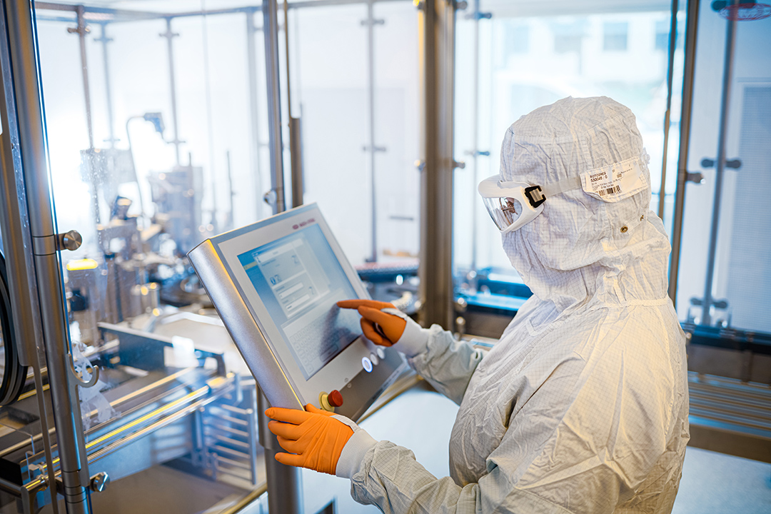 Mitarbeiter in Reinraumkleidung bedient über einen Touchscreen die automatisierte Anlage zur GMP-konformen Herstellung von Cold Kits bei ROTOP