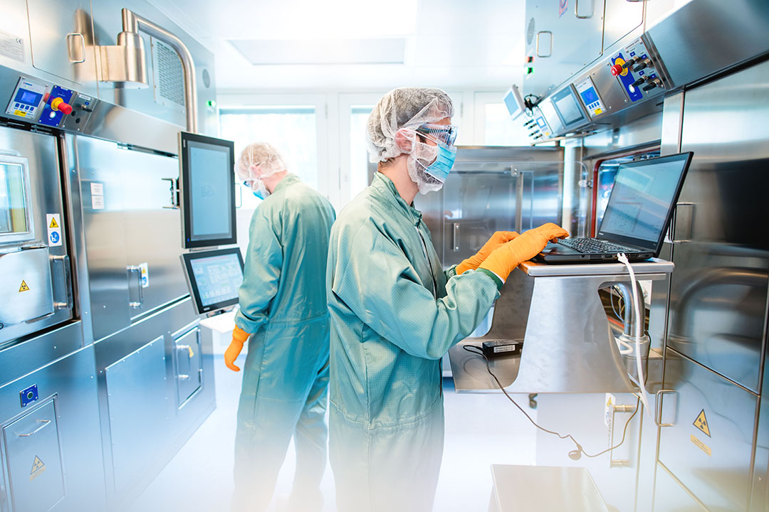 In einem modernen Reinraum der ROTOP Radiopharmacy überwachen zwei Mitarbeiter in Schutzkleidung die GMP-konfrome, automatisierte Herstellung von radioaktiven Arzneimitteln